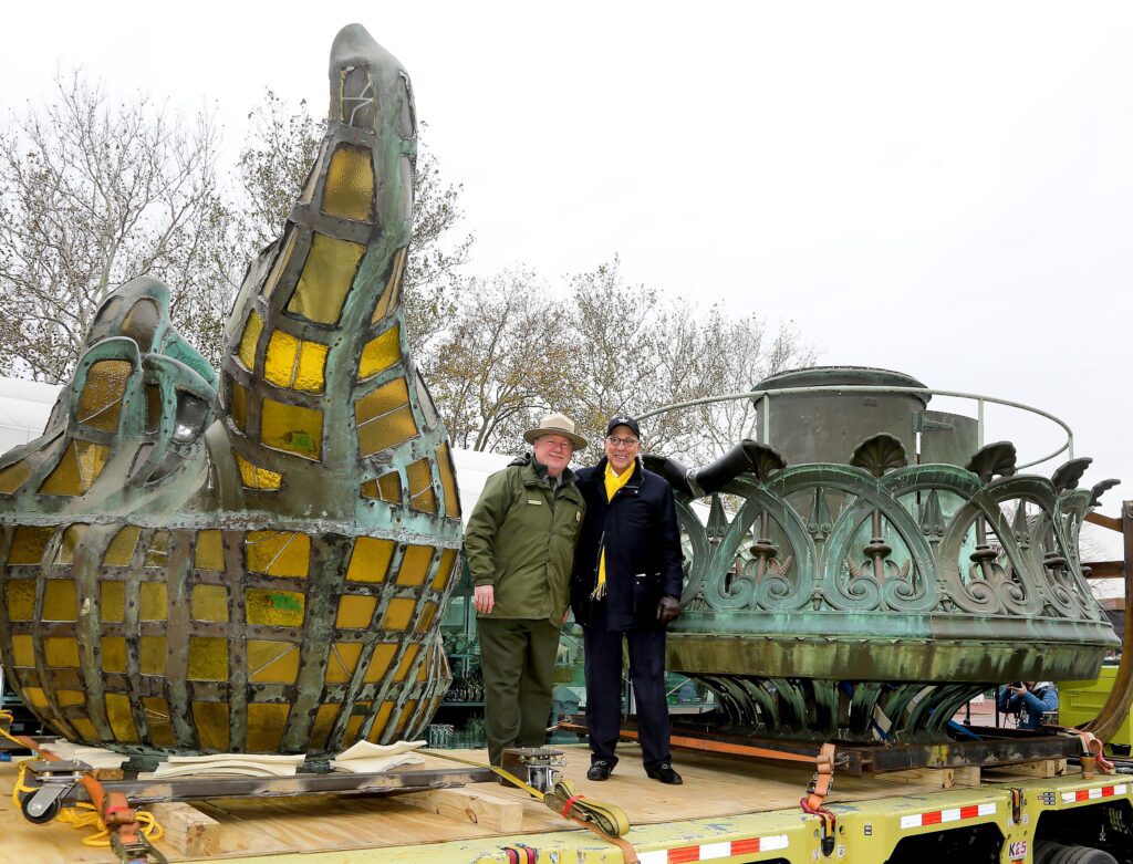 Two people standing next to the Statue of Liberty’s torch in the restoration process.