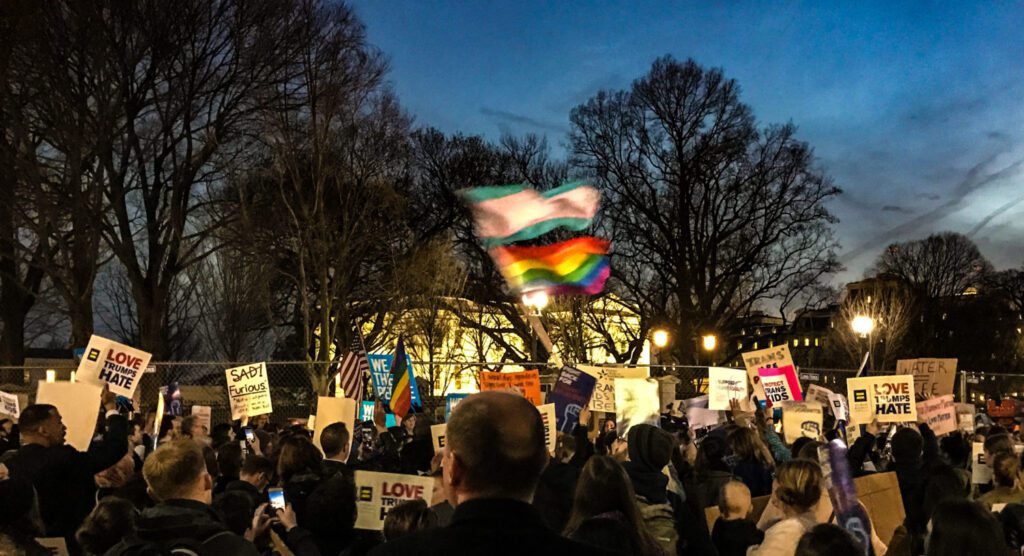Advocates holding signs and raising Pride flags in support of LGBTQ+ rights.