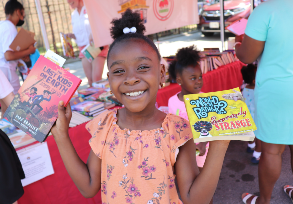 a smiling girl holds two books aloft.