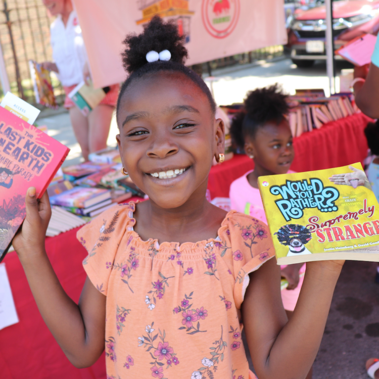 a smiling girl holds two books aloft.