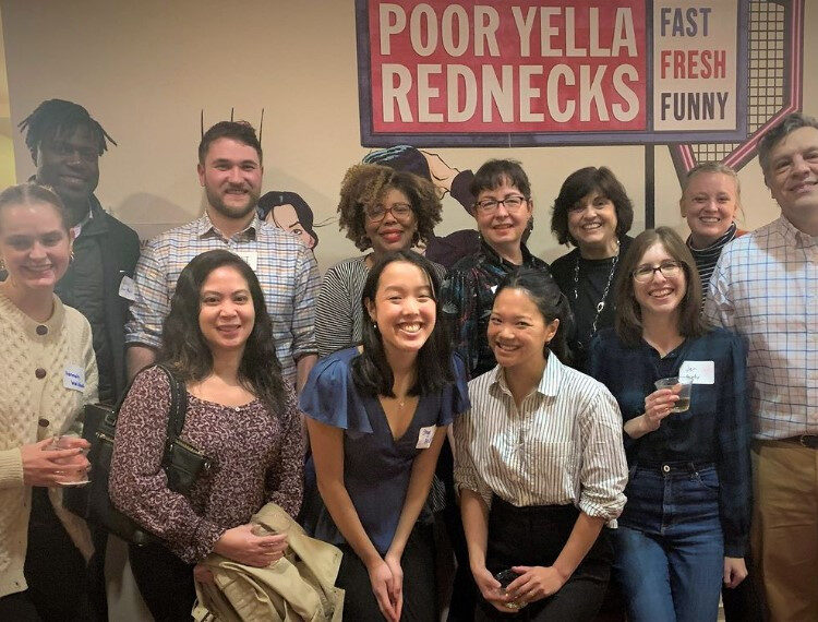 A group of theater-goers stand under a sign announcing the play title, Poor Yella Rednecks