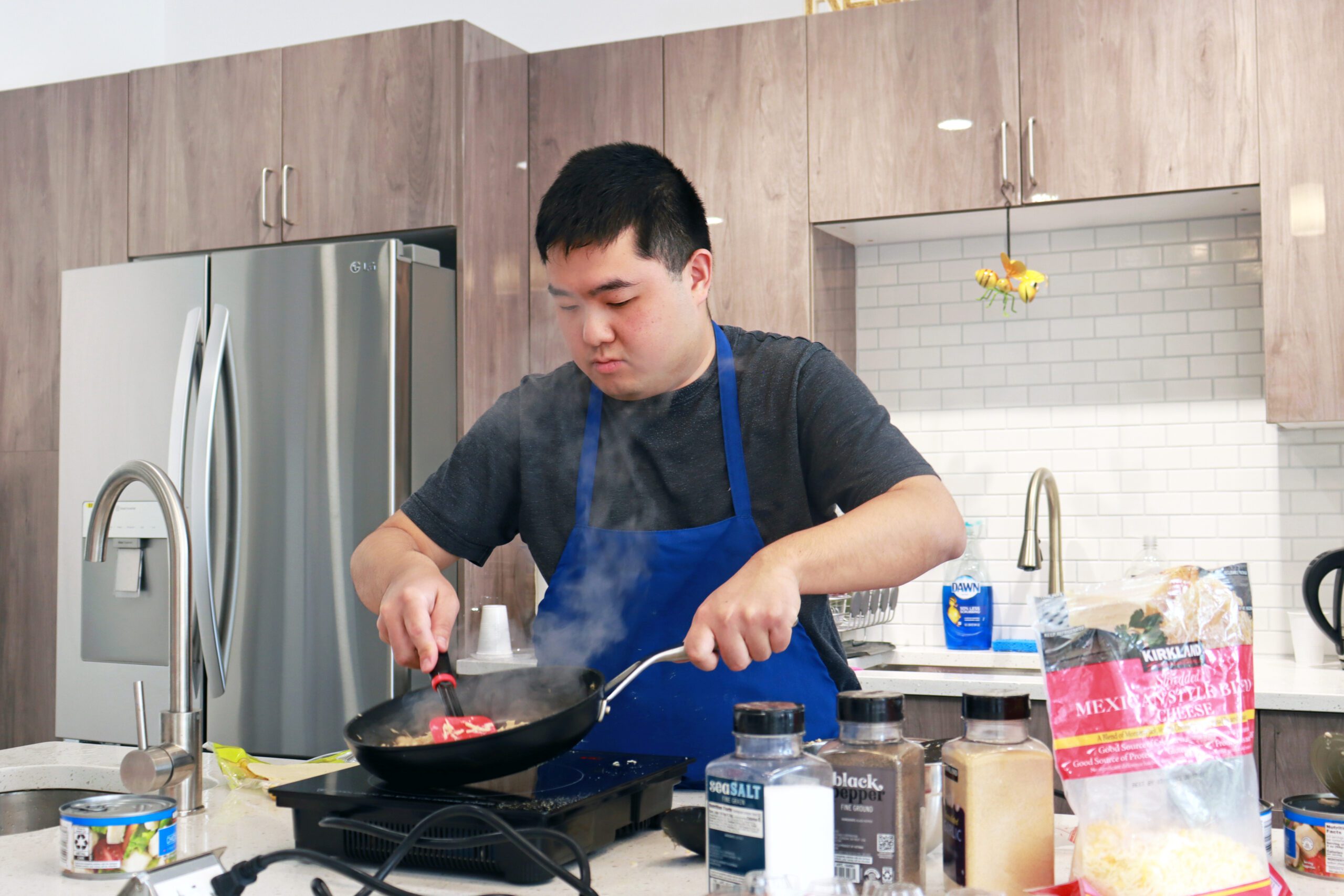 A young program participant wearing an apron cooks over a stovetop.