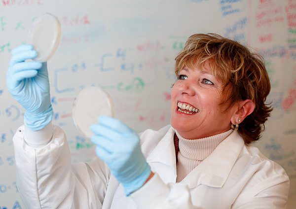 A person in a lab coat holds up discs and smiles.