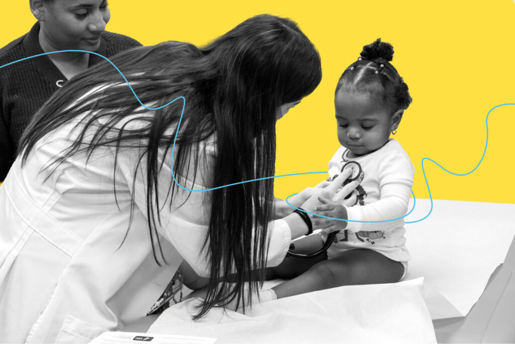 A doctor listens to a baby’s heartbeat through a stethoscope while a caregiver stands by.