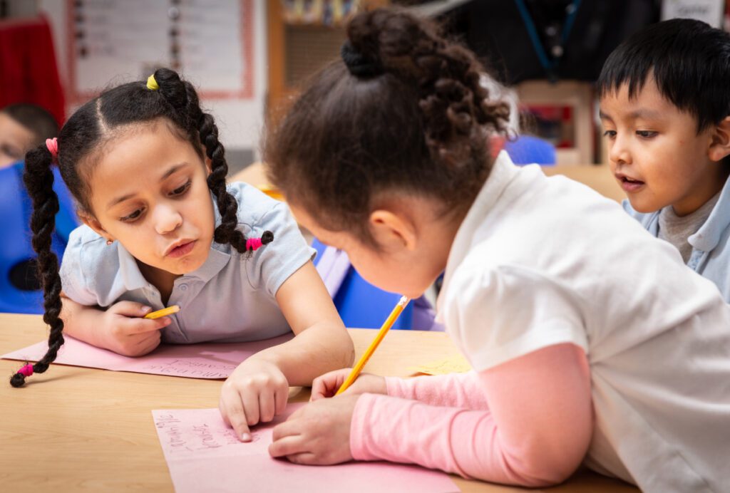 Three early elementary school students around a desk writing