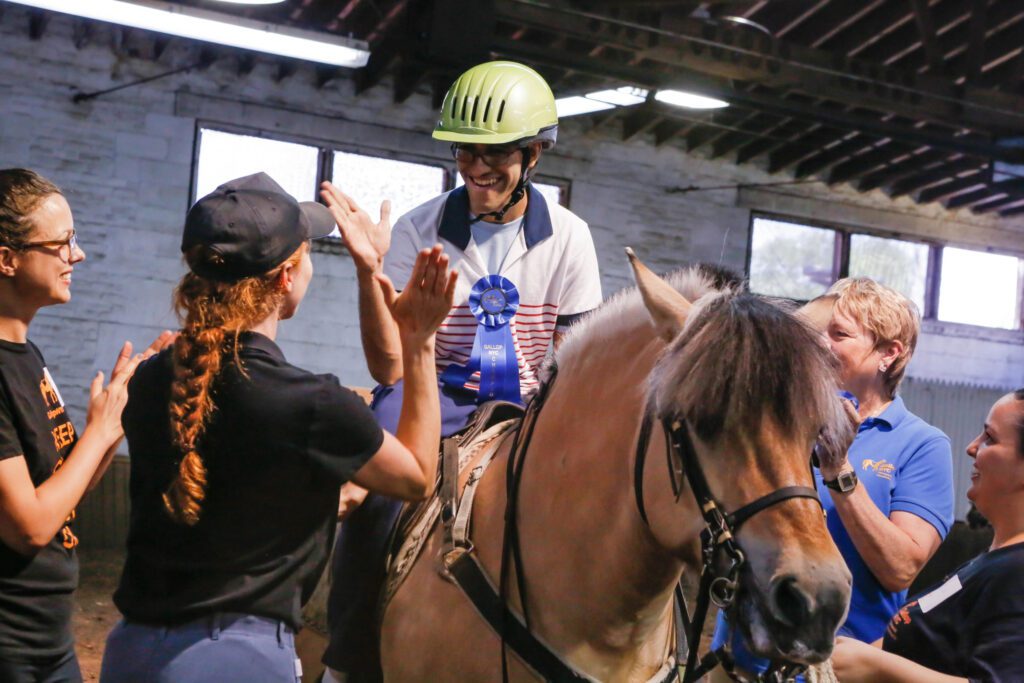 A horse rider sits atop a horse as a group of people applaud.