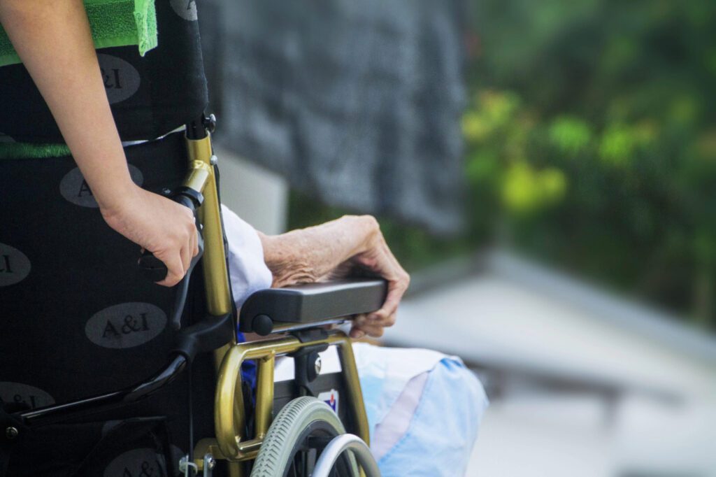A young person pushing an older adult in a wheelchair.